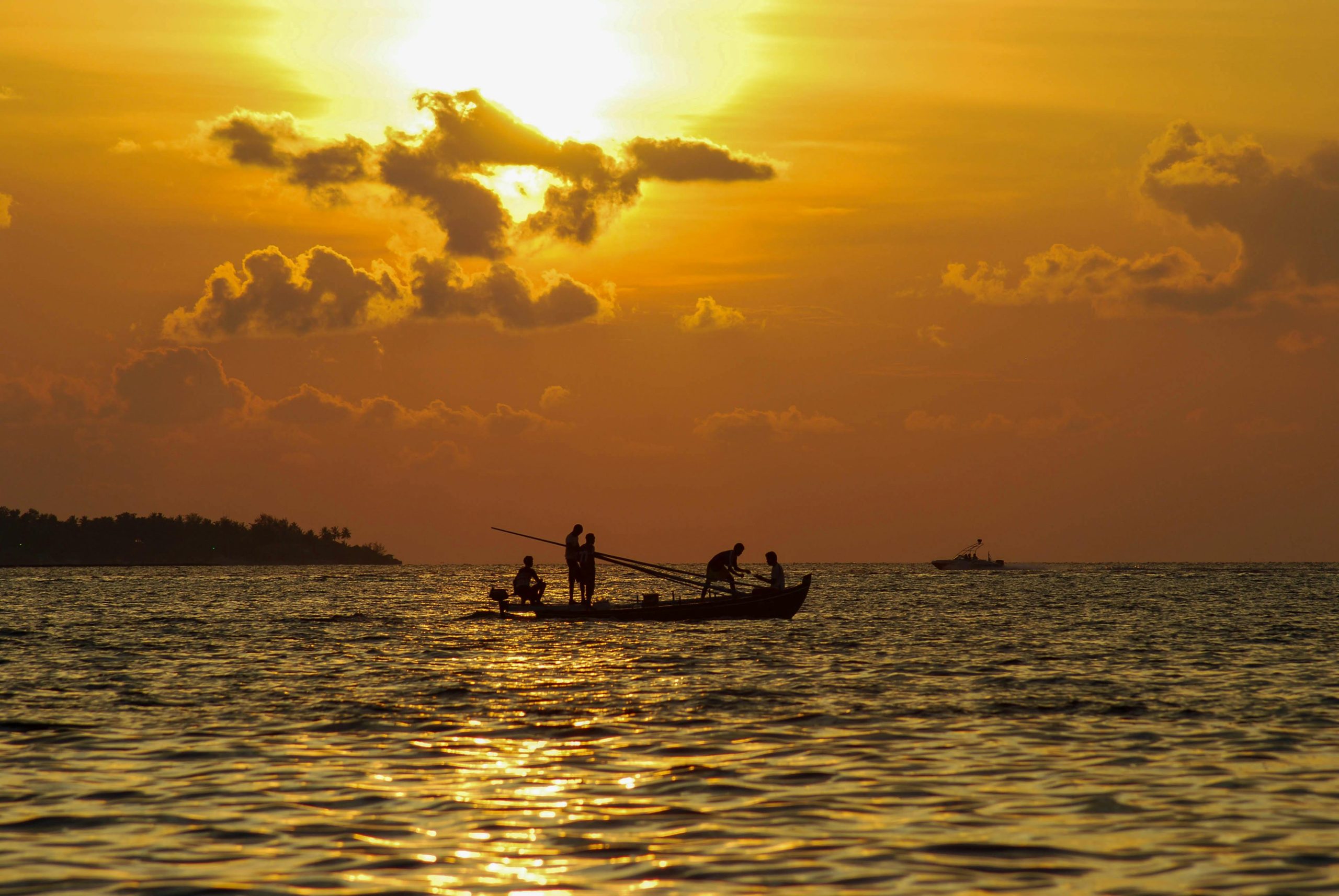 Silhouetted fishermen on a boat during a golden sea sunset in the Maldives.