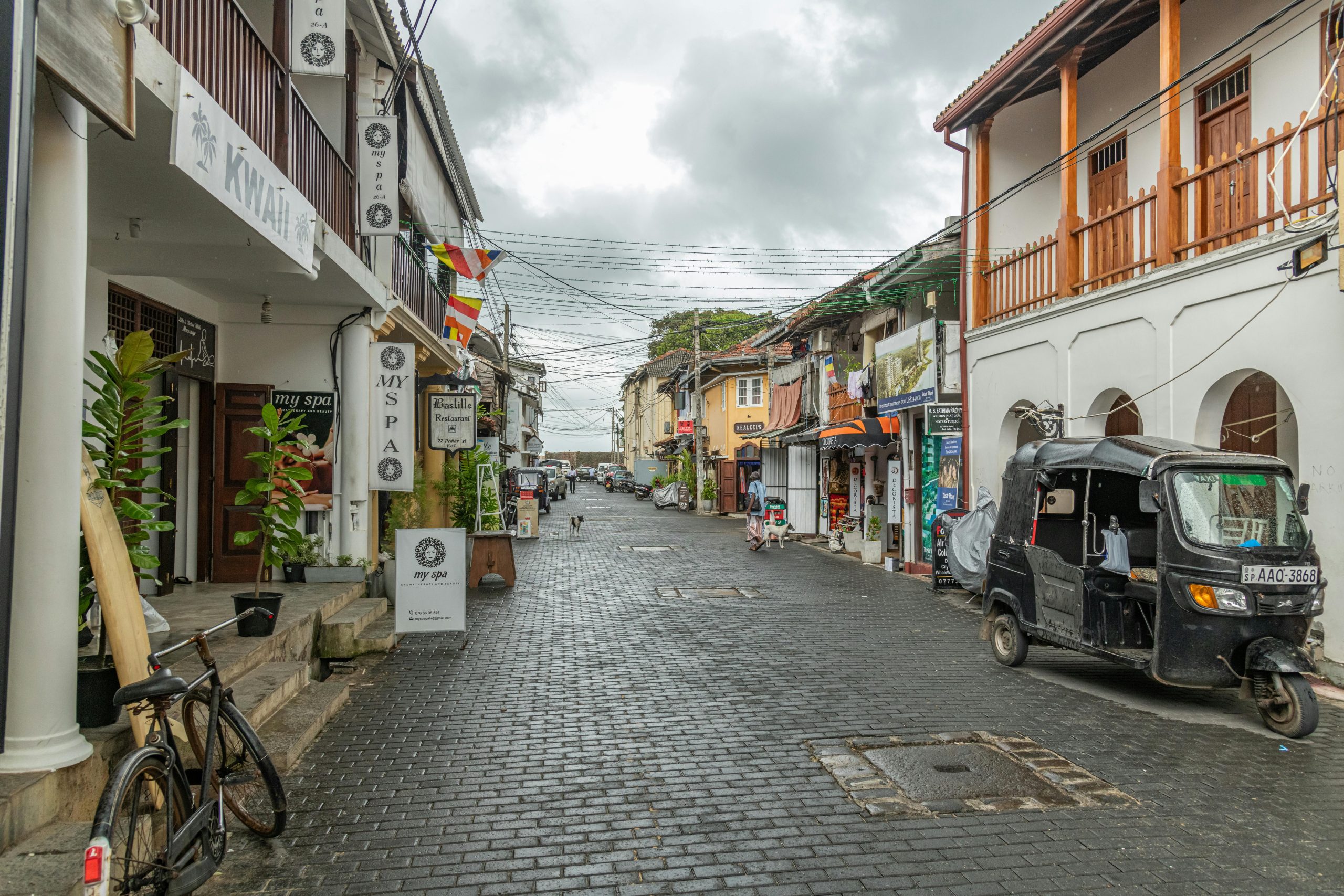 Scenic view of a cobblestone street with a black tuk-tuk in urban setting.
