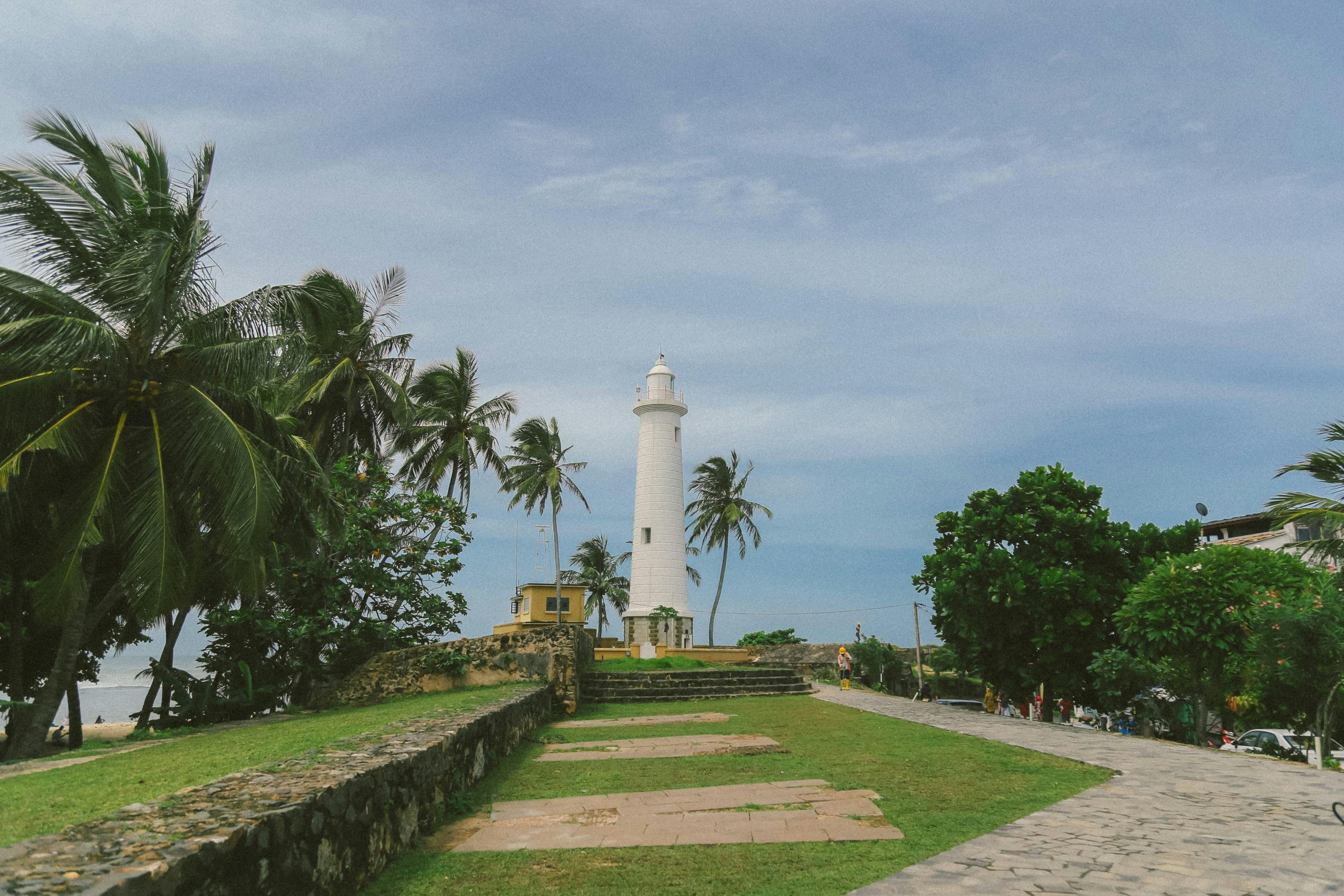 Scenic view of Galle Lighthouse surrounded by tropical palm trees and blue sky in Sri Lanka.